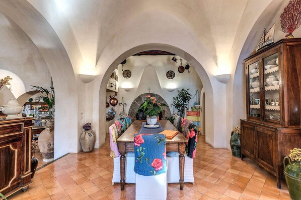 Une cuisine spacieuse avec un plafond en arc de cercle, une table à manger entourée de chaises et un buffet aux portes vitrées.