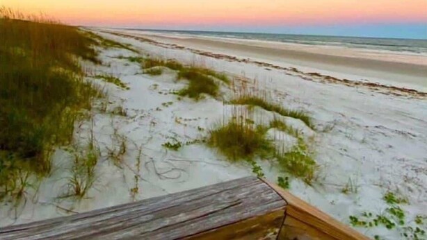 A beach with a wooden boardwalk leading to the water, sandy dunes, and a clear sky. - Salt & Sun - Beach & Pool (St. Augustine)