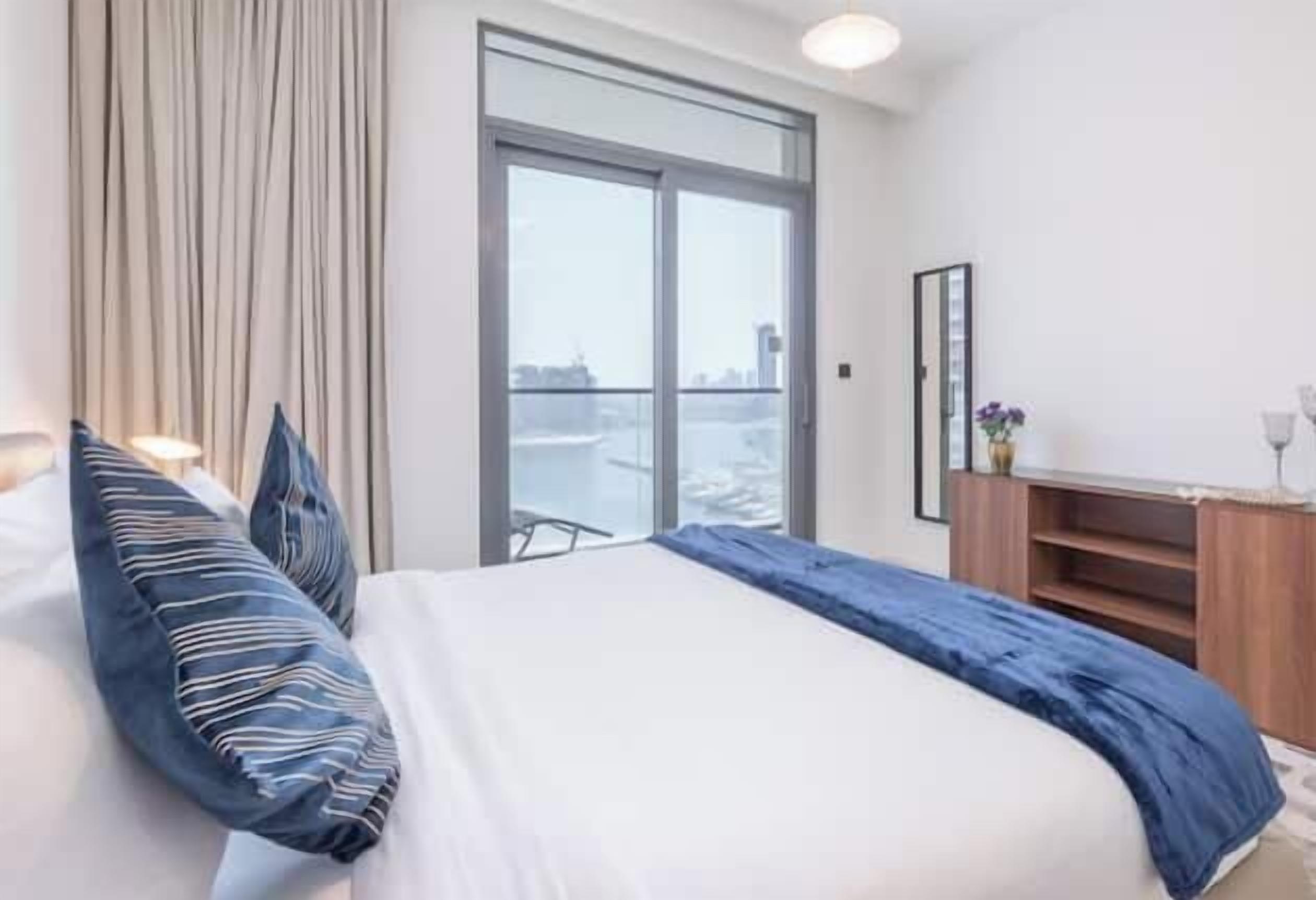 A hotel room with a large bed, a view of the city, a wooden dresser, and a curtain.