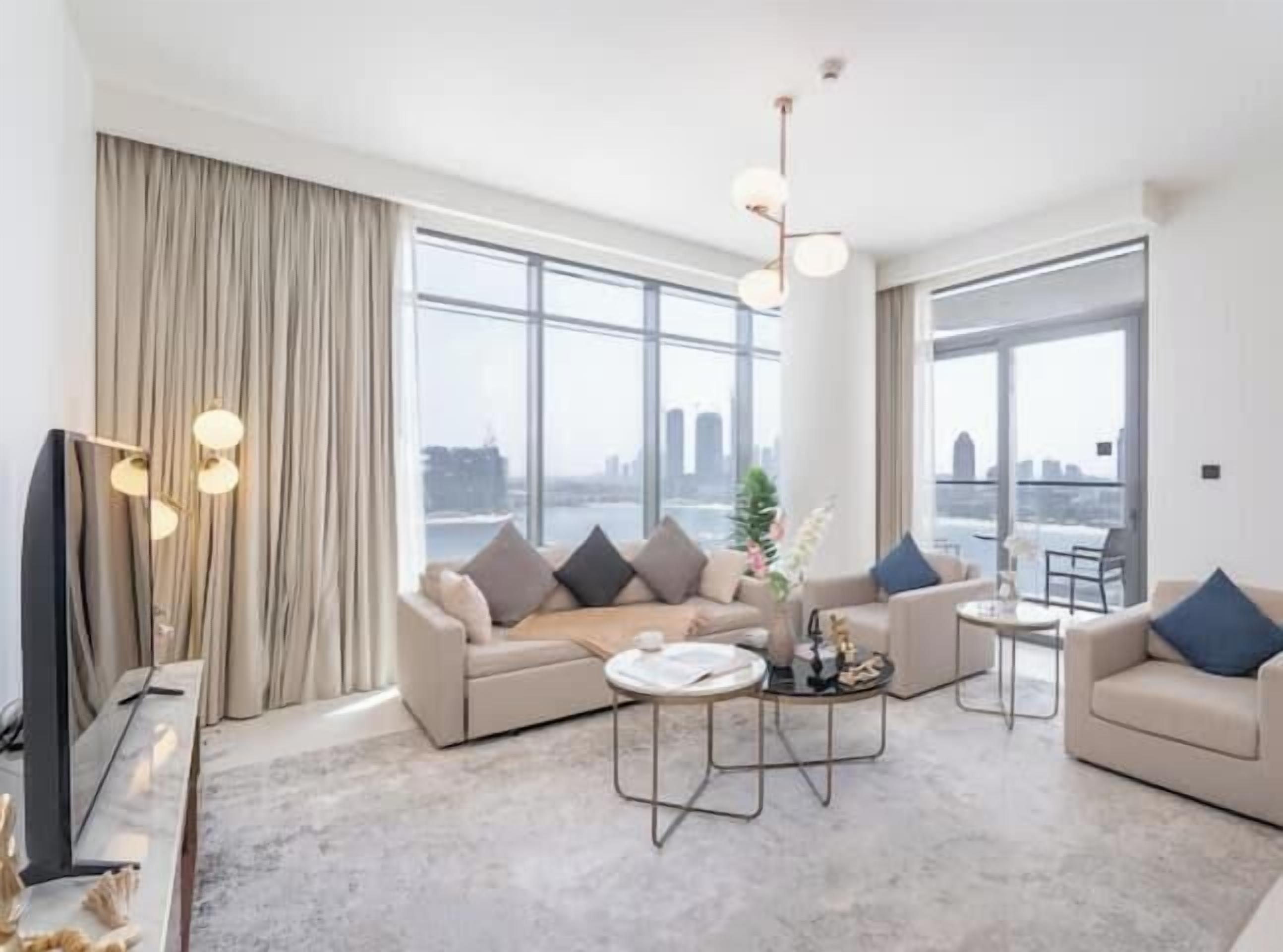 A modern living room with a sofa set, a coffee table, and a TV. Large windows offer a city view.