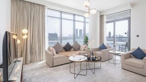 A modern living room with a sofa set, a coffee table, and a TV. Large windows offer a city view.