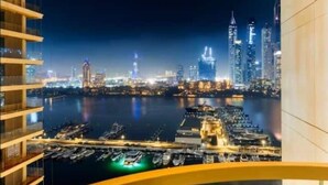 A night view of a city skyline with illuminated buildings and a marina with boats.