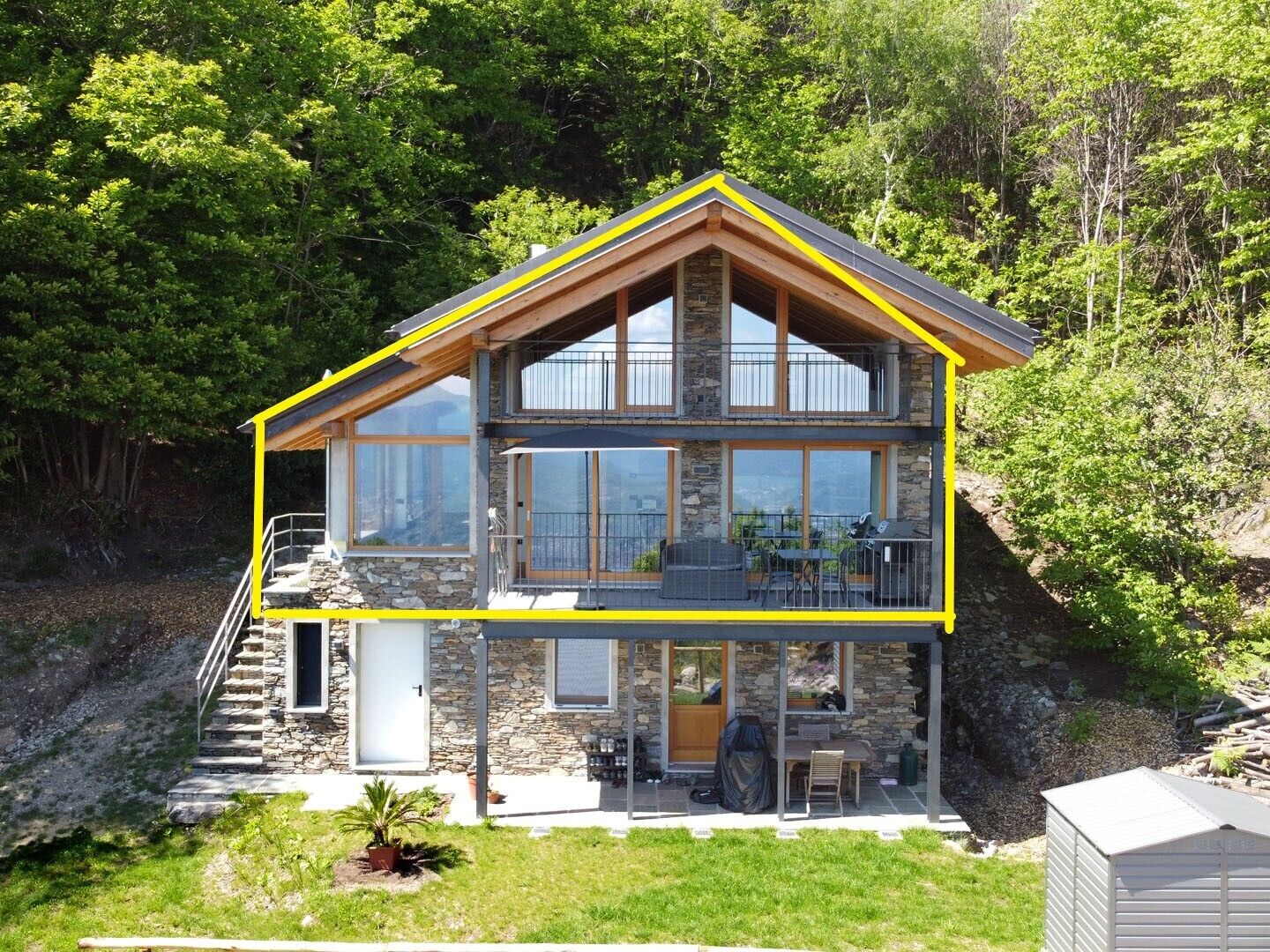 Une maison à deux étages avec une façade en pierre, de grandes fenêtres et un balcon.