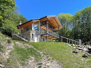 A modern two-story house with a stone foundation, wooden beams, and a balcony. - Rustico Milu’ (Viggiona)