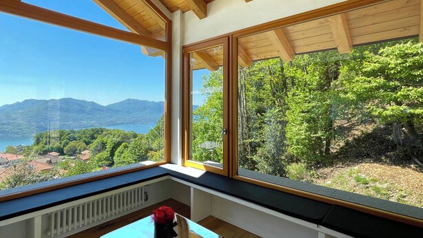 A room with large windows offering a view of a lake and mountains. - Rustico Milu’ (Viggiona)