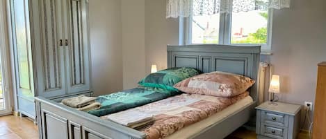Classic bedroom with a large bed, bedside tables, and a window with a lace curtain.