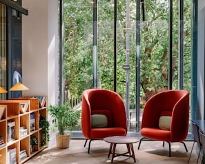 A modern room with two red chairs, a small round table, and a bookshelf with books and a potted plant. - Student Only Scape Leeds (Leeds)