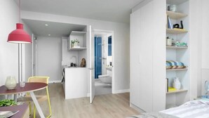 Ein modernes Schlafzimmer mit Bett, Nachttisch und Ablagefläche. Ein Kleiderschrank mit Regalen und einem Spiegel ist vorhanden. Ein Badezimmer mit Dusche und Toilette ist sichtbar.