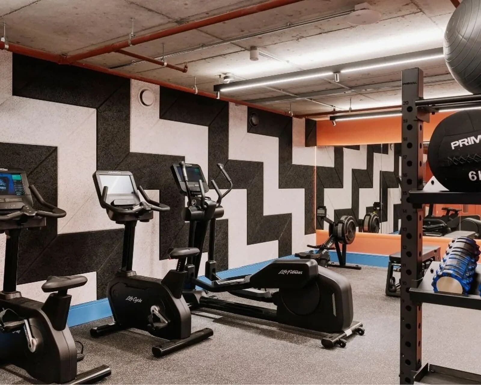 A gym with exercise equipment, a mirrored wall, and a weightlifting rack.