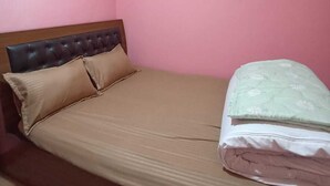Ein Einzelbett mit Kopfteil, zwei Kissen und einer gefalteten Decke in einem Zimmer mit rosafarbenen Wänden.