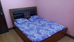 Ein Schlafzimmer mit einem Bettgestell aus Holz, einem gepolsterten Kopfteil und einer zudeckenden Bettwäsche mit Blumenmuster.