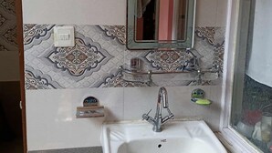 Ein Badezimmer mit gemusterten Fliesen, einem weißen Waschbecken, einem Spiegel und einem Fenster.