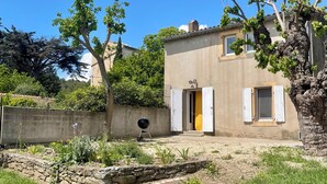 A two-story house with a stone wall, a barbecue grill, and a garden with various plants and a small pond. - Idyllic gîte with private pool and garden in beautiful surroundings. (Laure-Minervois)