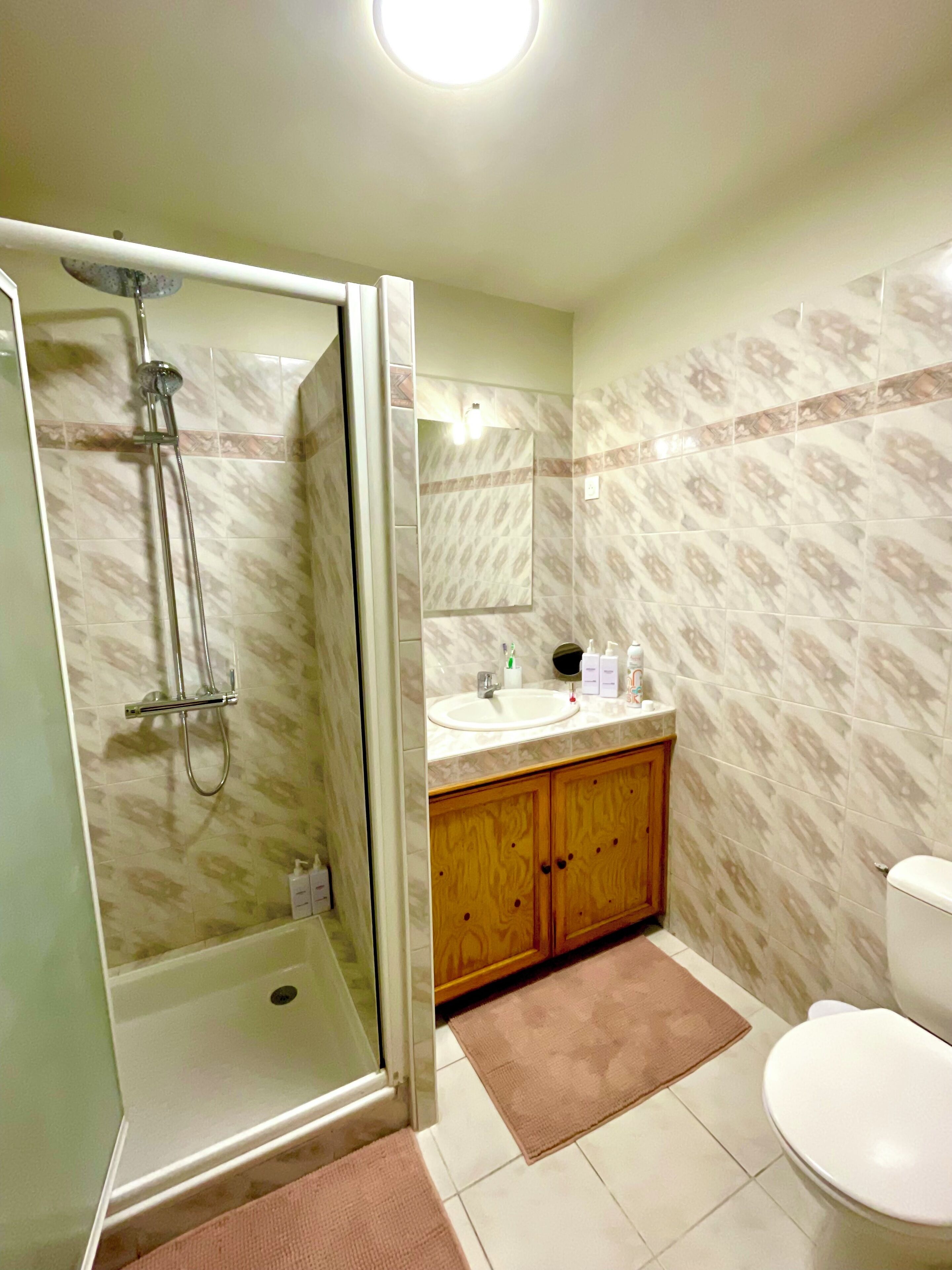 A bathroom with a shower, sink, toilet, and wooden cabinets.