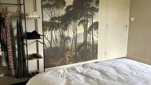 A bedroom with a large bed, a wardrobe, a clothing rack, and a painting of trees. - Idyllic gîte with private pool and garden in beautiful surroundings. (Laure-Minervois)