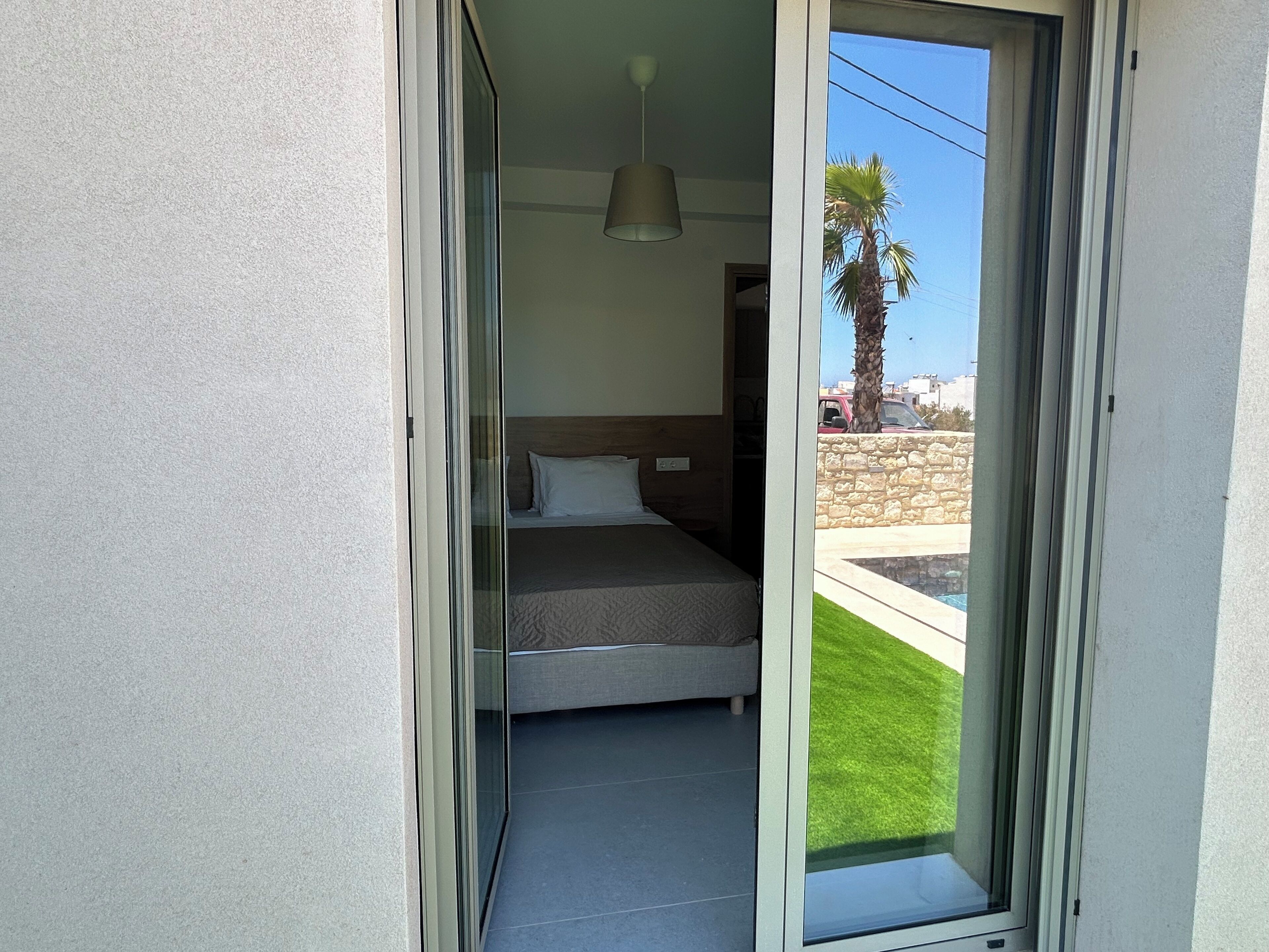Una camera da letto con un letto, una lampada a sospensione e vista su una palma e una piscina.