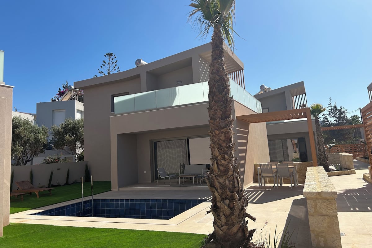 A modern two-story house with a swimming pool, outdoor seating, and a palm tree.
