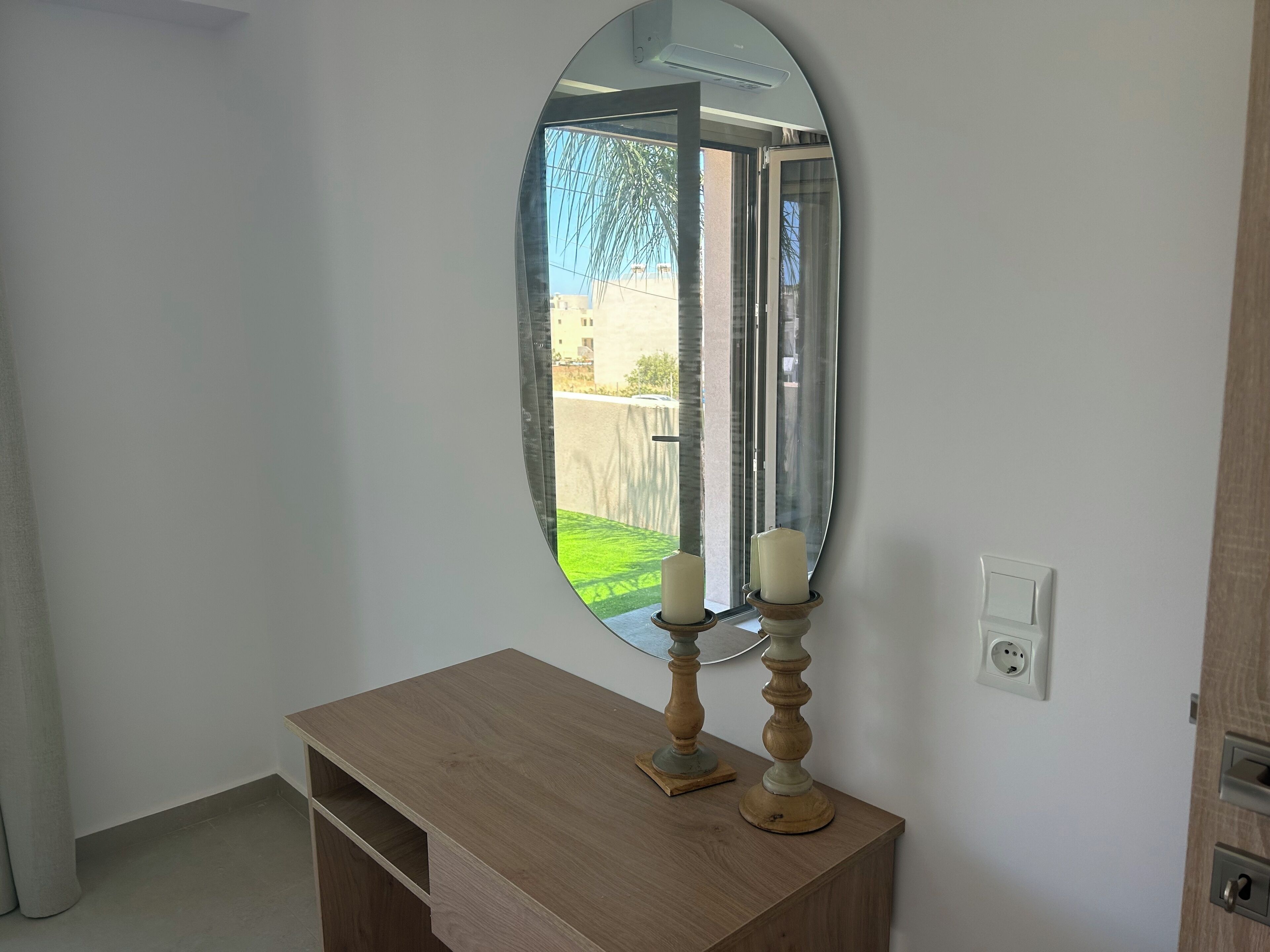 A room with a wooden dresser, a mirror, and a wall socket.