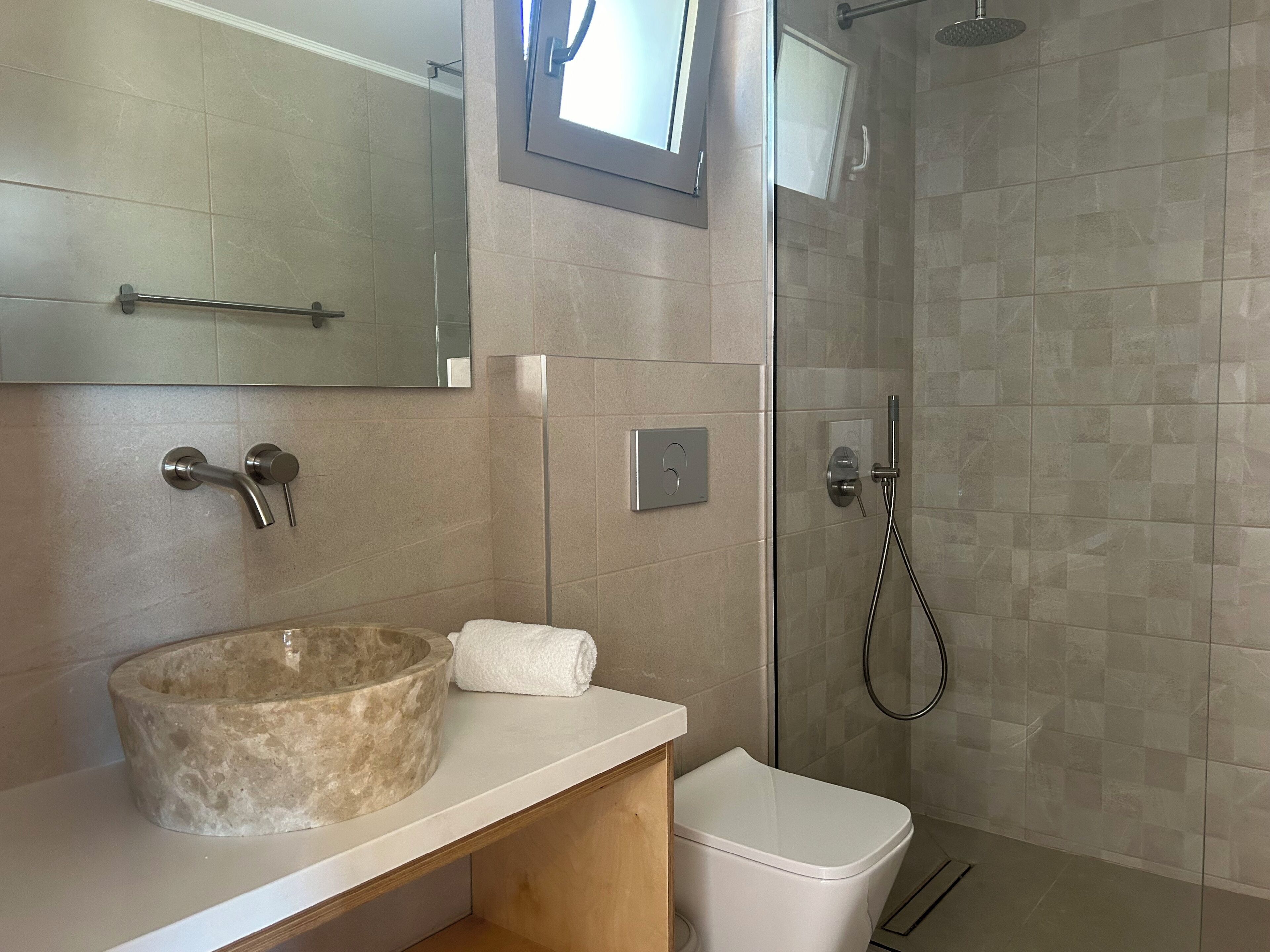 Un baño con un lavabo de piedra, inodoro, ducha con puerta de cristal y espejo sobre el lavamanos.