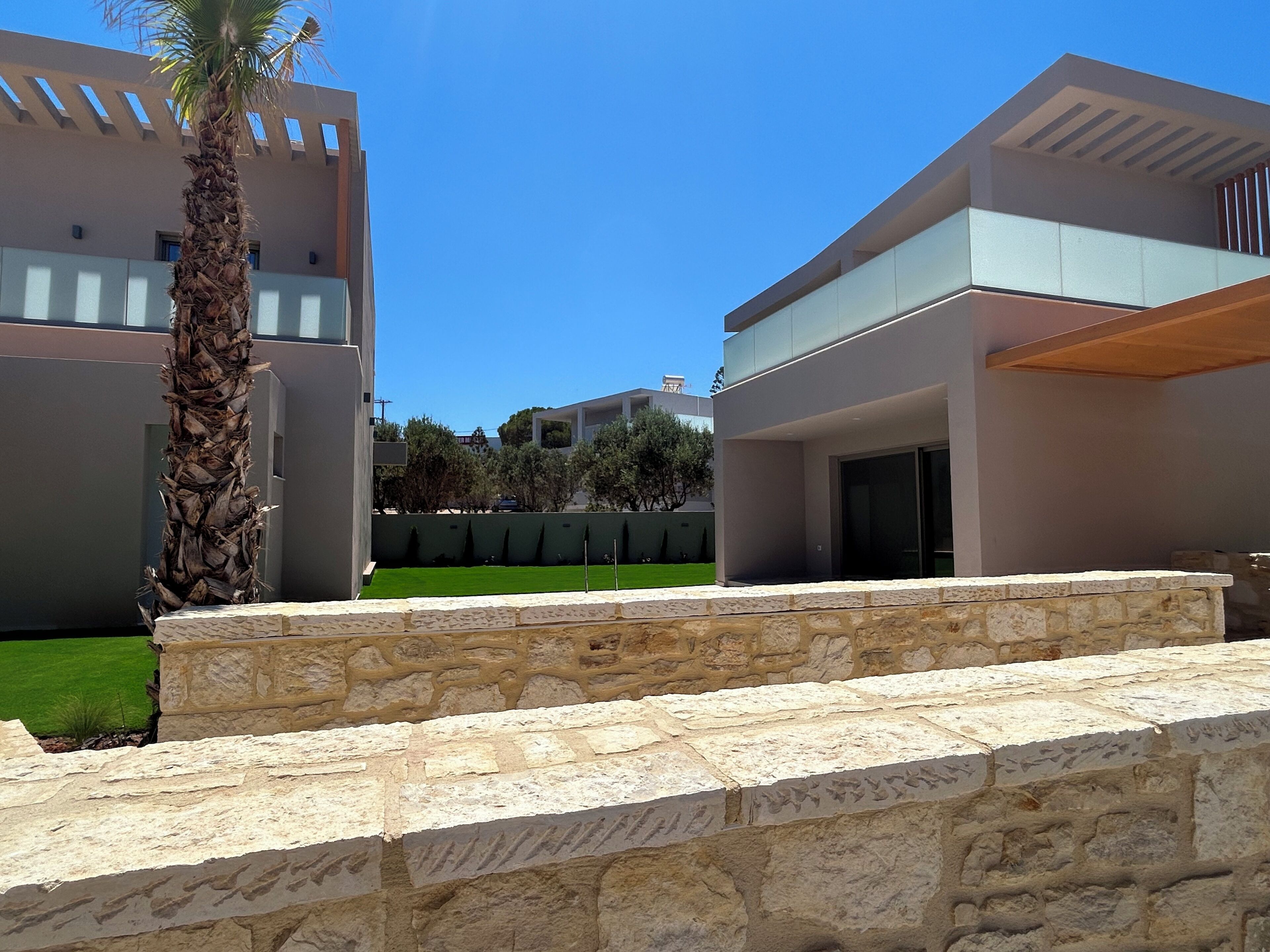 A modern building with a stone retaining wall and a palm tree.