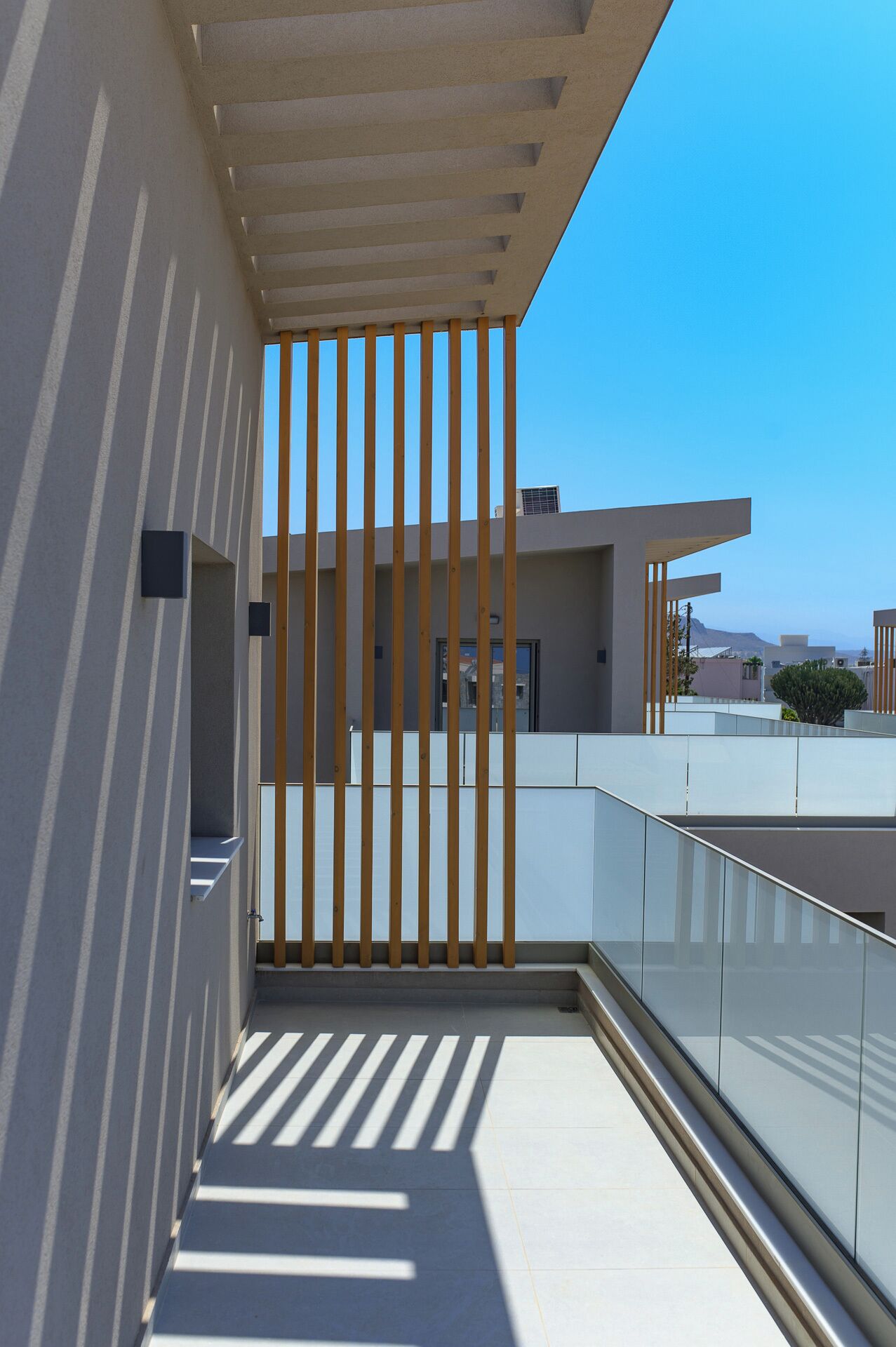 A modern building with a balcony, wooden slats, and a clear blue sky.