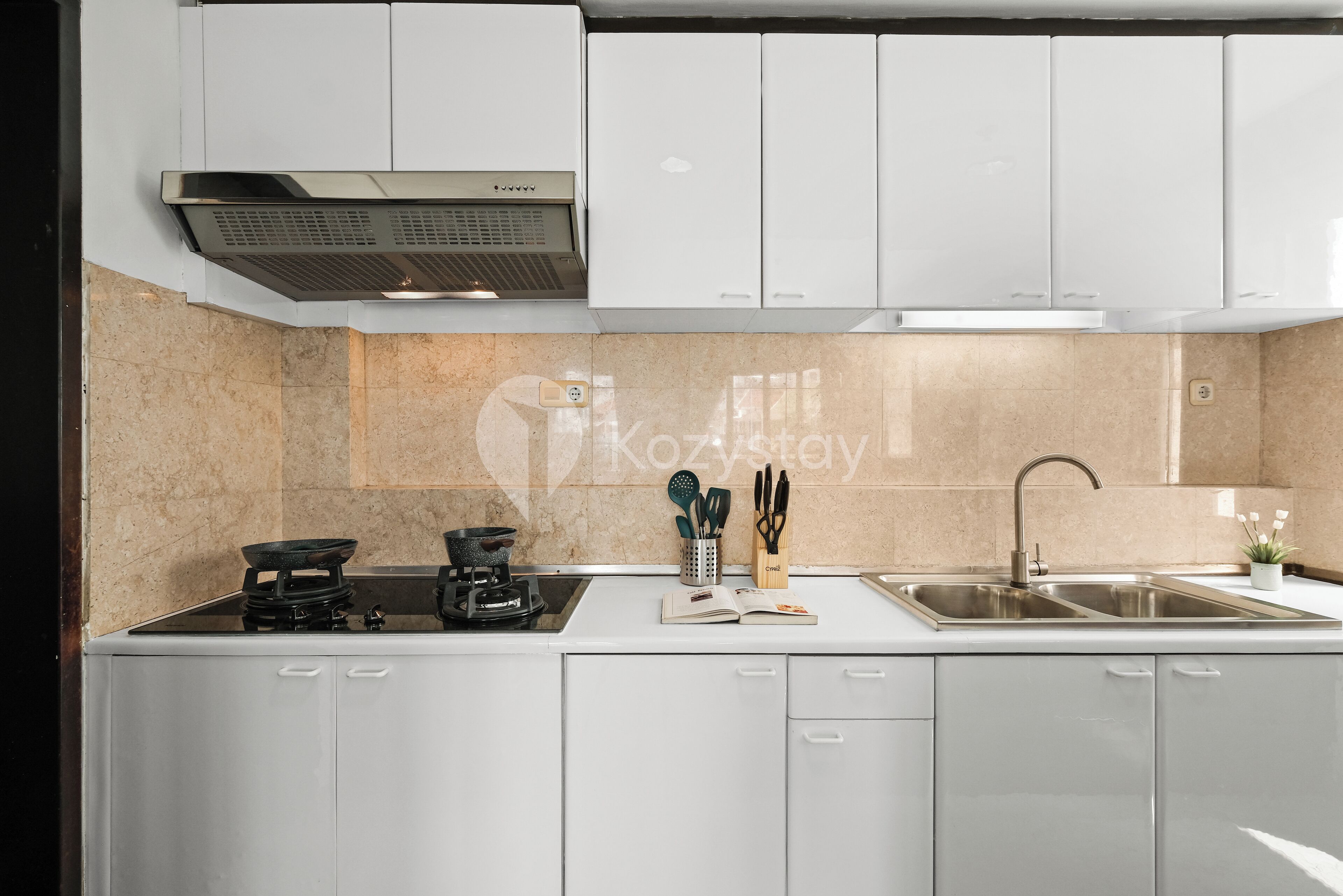 Una cocina moderna con gabinetes blancos, estufa integrada, cafetera y un lavamanos.