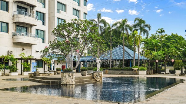 A hotel courtyard with a swimming pool, palm trees, and a building with balconies. - Beleria by Kozystay - Senayan (Jakarta)