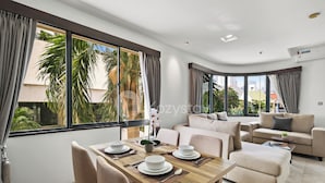 A modern living room with a dining area, large windows, and a view of palm trees. - Beleria by Kozystay - Senayan (Jakarta)