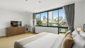 A modern hotel room with a large bed, a TV on a wooden cabinet, and a view of the cityscape through large windows. - Beleria by Kozystay - Senayan (Jakarta)