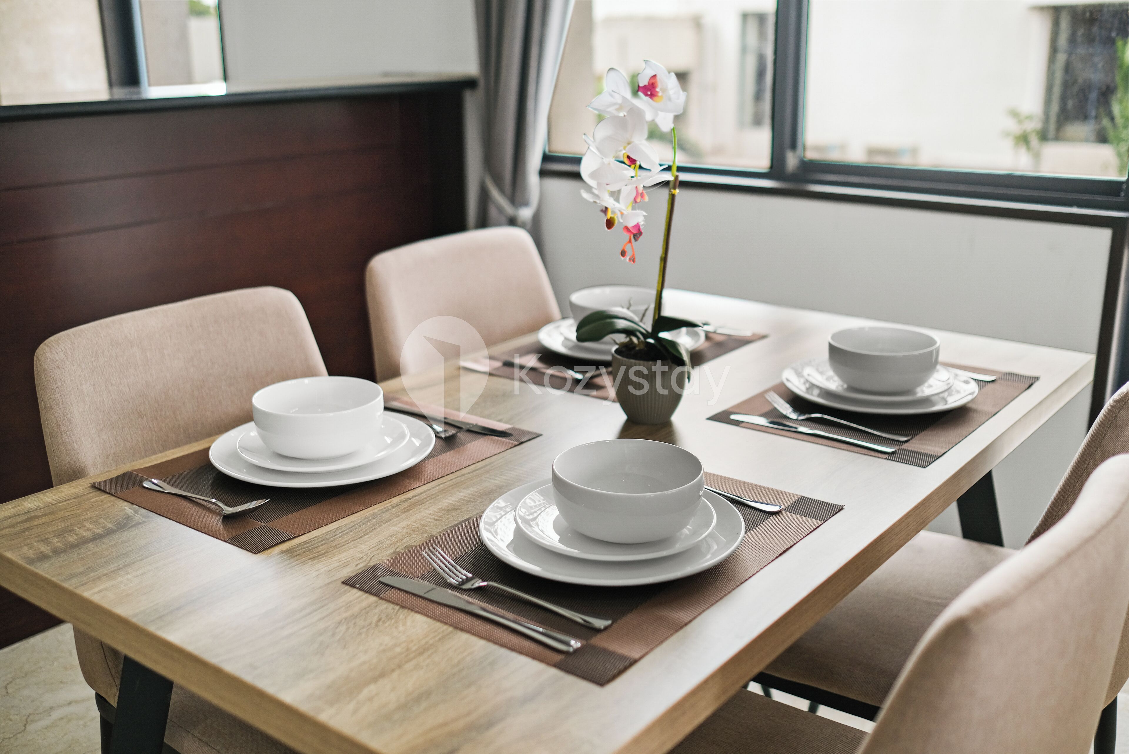 A dining table set with white bowls and plates, a vase with flowers, and a window view.