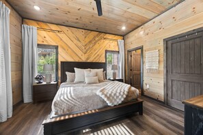 Un dormitorio con cama, mesitas de noche, ventana y puerta.
