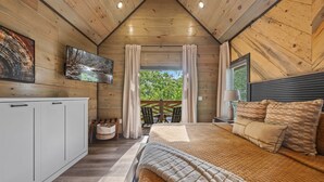 Un dormitorio acogedor con una cama grande, un televisor montado en la pared y vistas a zonas verdes.