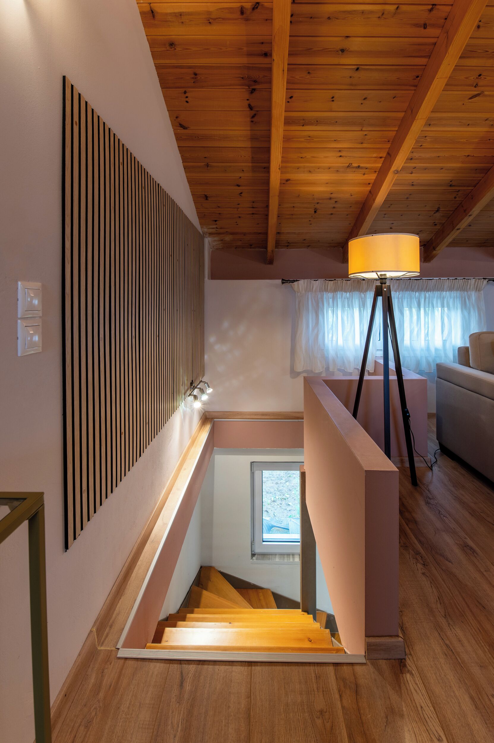 A staircase with wooden steps leading to a landing, a modern lamp, and a window with curtains.