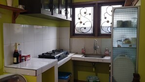 A compact kitchen with white tiles, a gas stove, a sink, and a window with decorative ironwork. - Ventera Homestay (Kalasan)