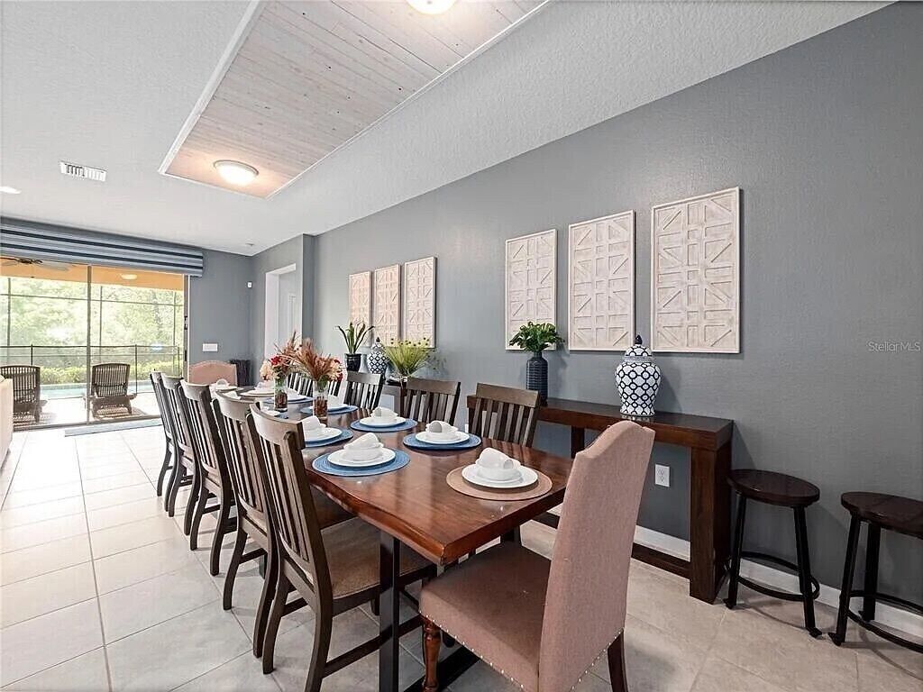 A dining area with a long wooden table set for six, surrounded by chairs. There are three wall-mounted decorative panels above the table.