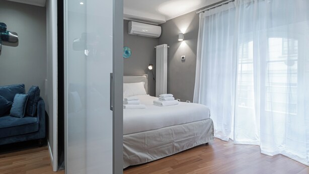 A modern bedroom with a bed, a blue sofa, and a glass door leading to another room. - Italianway - Solferino 33 (Milan)