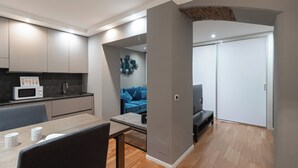 A modern kitchen with a microwave, sink, and cabinets. There is a dining table with chairs and a blue sofa in the living area. - Italianway - Solferino 33 (Milan)