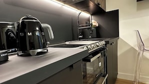 A modern kitchen with a sleek black countertop, a coffee maker, a kettle, and a stove. - Paris Marais by Melvane (Paris)