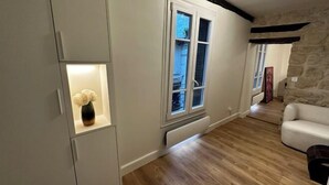 A room with a white cabinet, a white sofa, a stone wall, and a window with a view of the outside. - Paris Marais by Melvane (Paris)