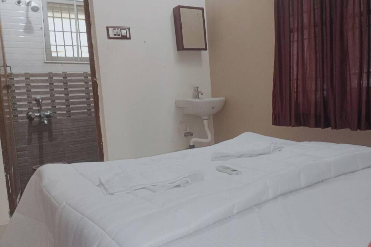 A hotel room with a bed, a white sink, a mirror, and a window with curtains.