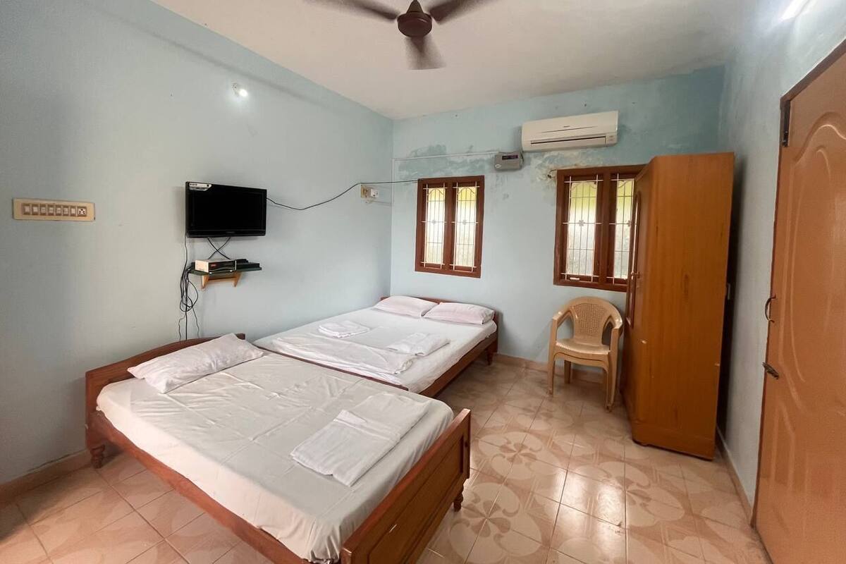 A room with two beds, a ceiling fan, an air conditioner, a TV, and a window with bars.