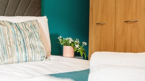 A neatly made bed with striped pillows, a small potted plant, and a wooden wardrobe. - Modern 2 Bed apartment in Liverpool, City Centre (Merseyside)