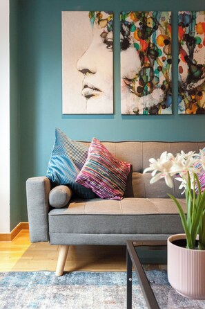 A modern living room with a grey sofa, colorful pillows, a small side table, and a potted plant.