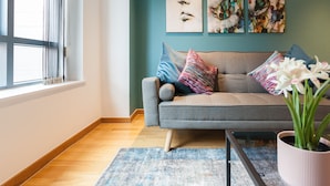 A modern living room with a grey sofa, colorful pillows, a blue rug, and a potted plant. - Modern 2 Bed apartment in Liverpool, City Centre (Merseyside)