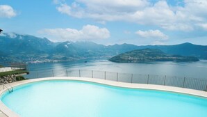 Une grande piscine aux eaux cristallines, offrant une vue sur les montagnes et un plan d’eau en arrière-plan.