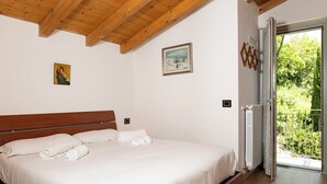 Une chambre à coucher avec un cadre de lit en bois, du linge de lit blanc, un tableau au mur et, par une porte ouverte, une vue sur un balcon.