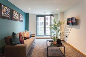 A living room with a sofa, a coffee table, a TV, and a door leading to a balcony. - Modern 2 Bed Flat in Liverpool City Centre (Merseyside)