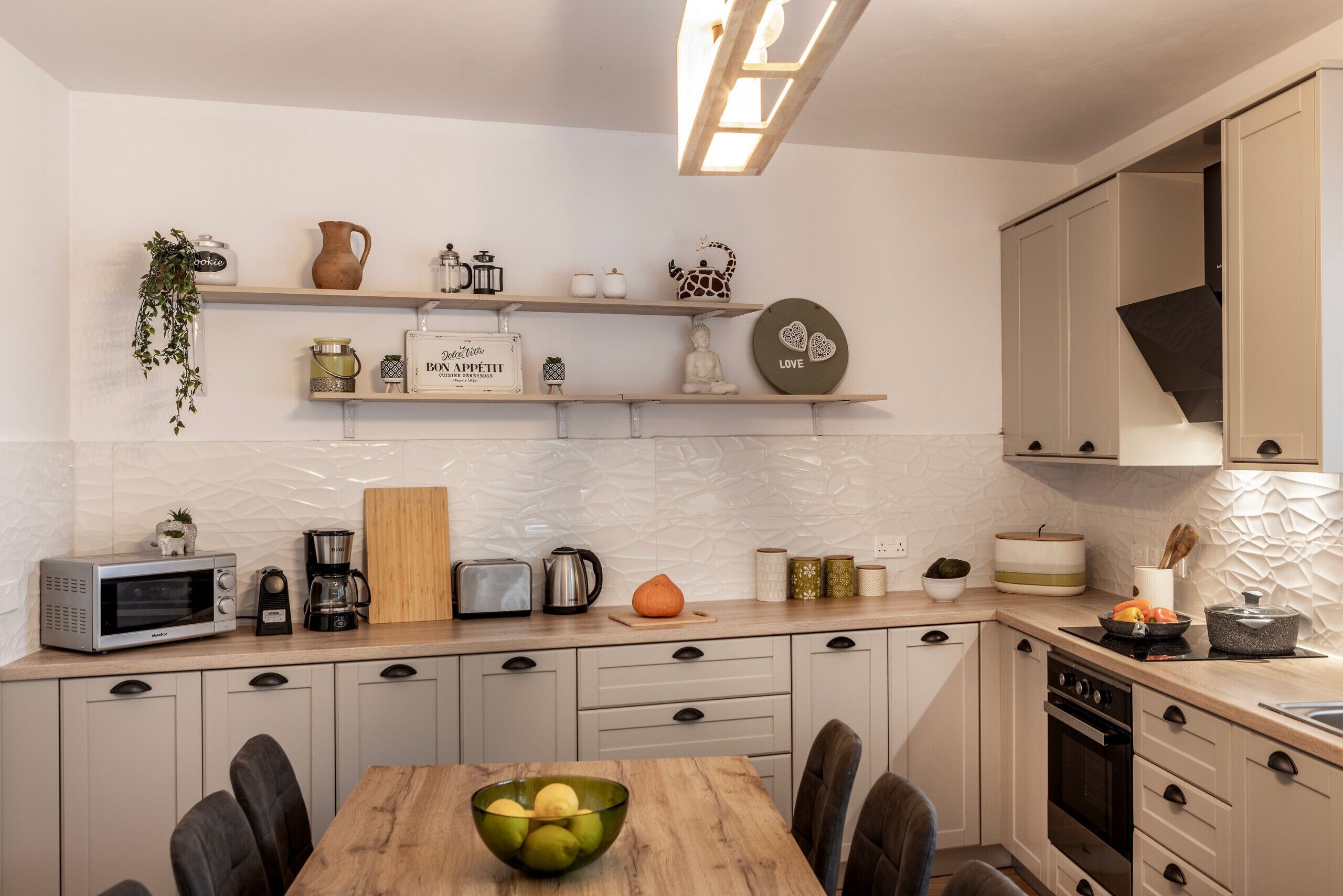 Une cuisine moderne avec une table à manger en bois, des appareils électroménagers intégrés et des objets décoratifs disposés sur des étagères.