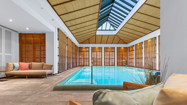 A modern indoor swimming pool with a glass barrier, wooden sliding doors, and a high ceiling with natural light. - Luxury apartment with balcony, free SPA use and gym (Sylt)