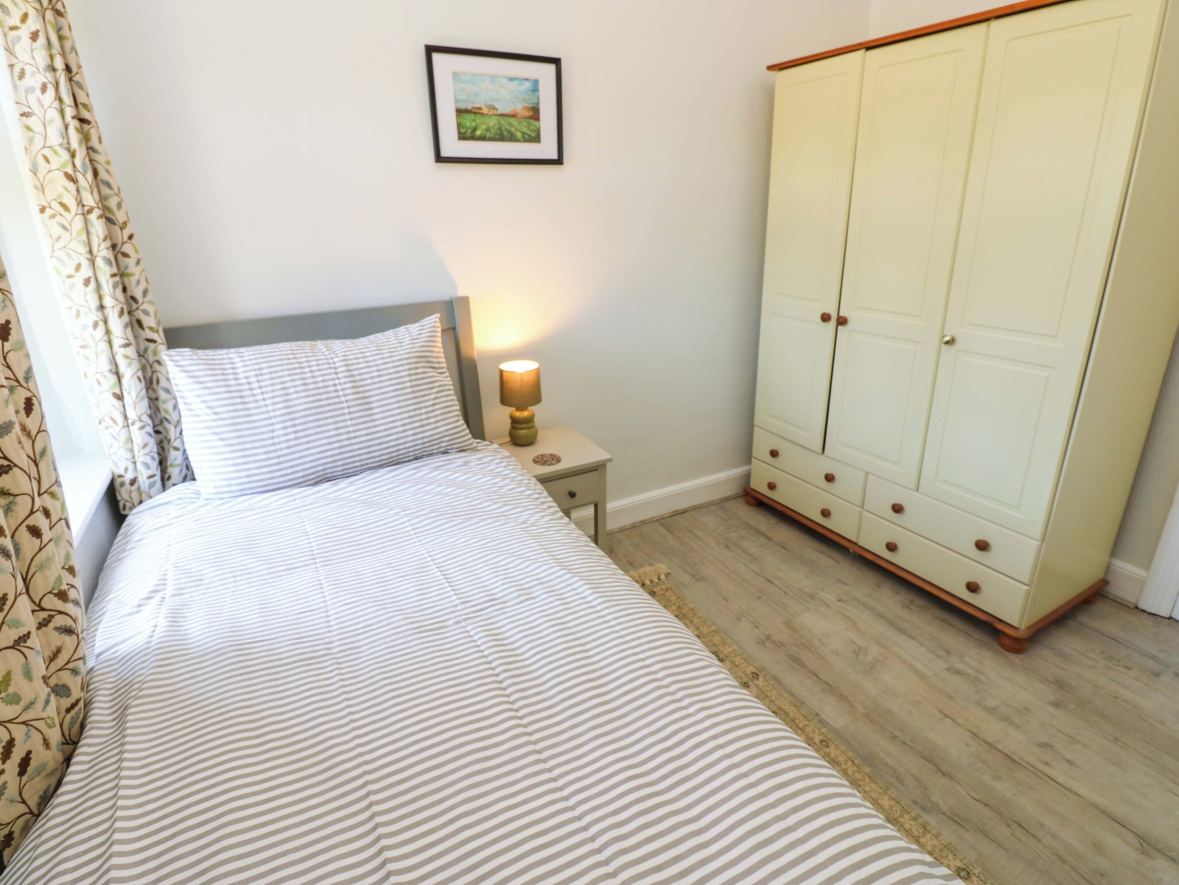 A bedroom with a bed, a nightstand, a lamp, a wardrobe, and a framed picture on the wall.